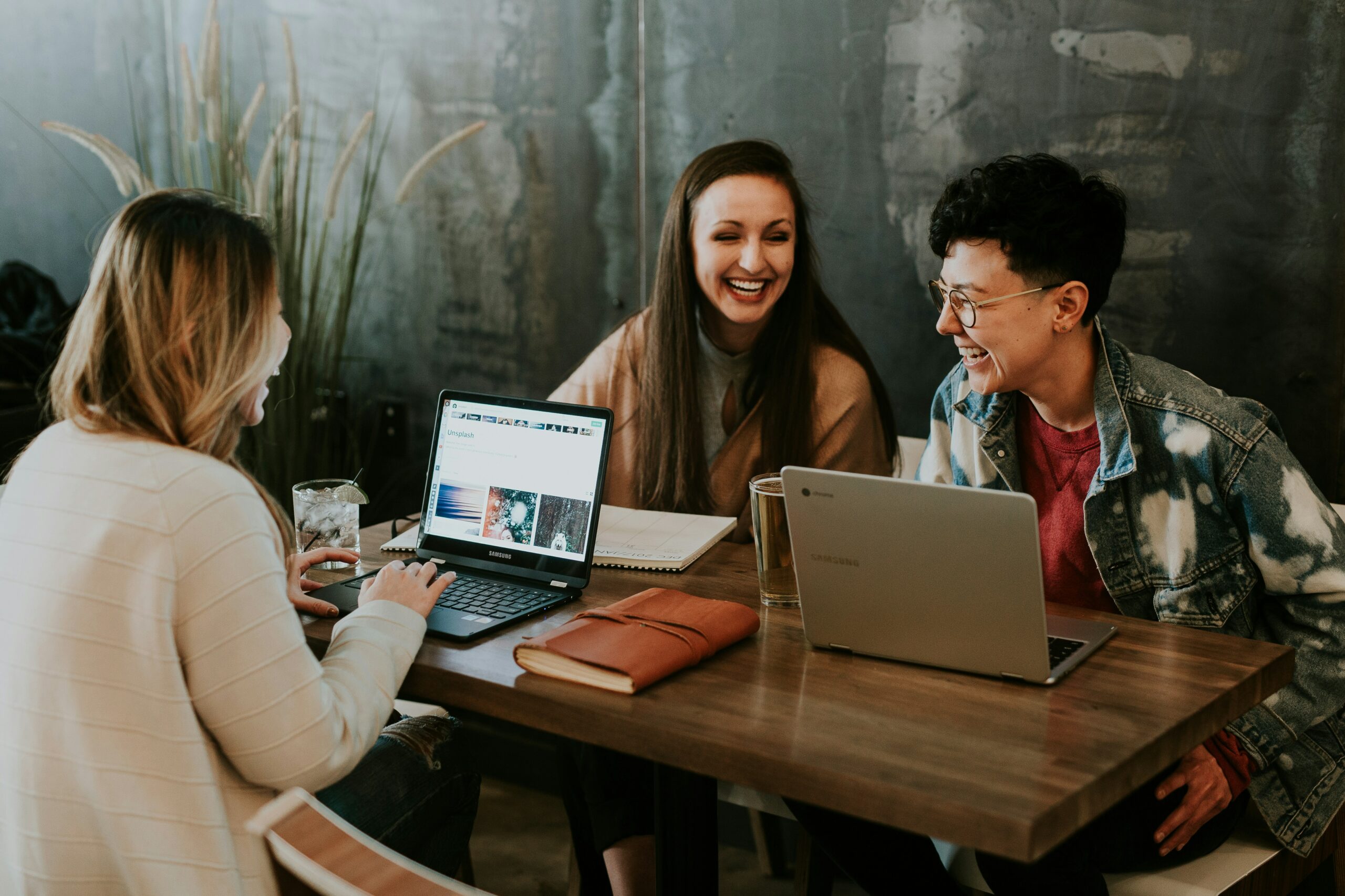 Trois jeunes adultes souriants travaillant ensemble sur des ordinateurs portables autour d’une table